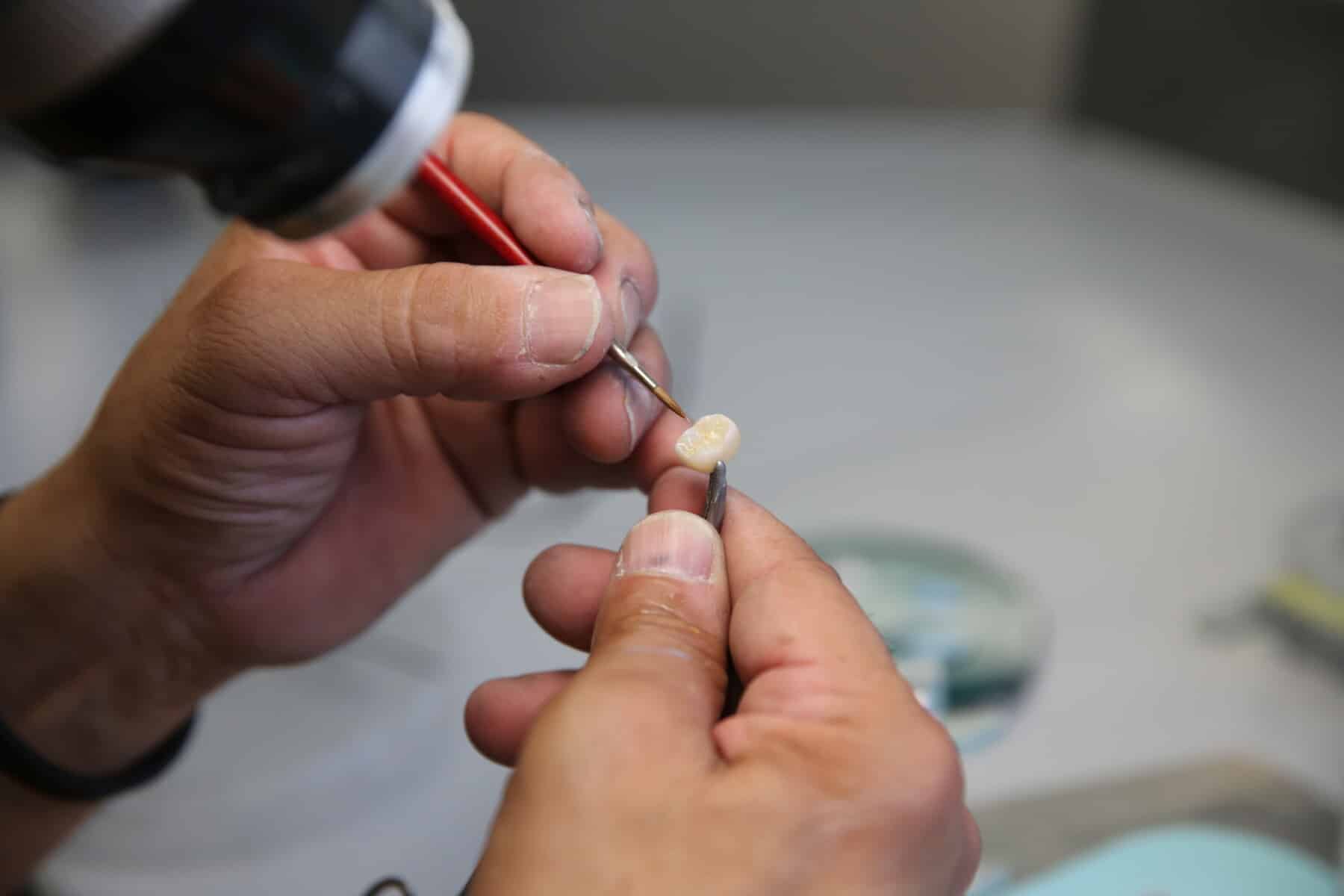 Close-up of a technician hand-crafting a porcelain dental crown, applying final details for superior aesthetics and a natural look.