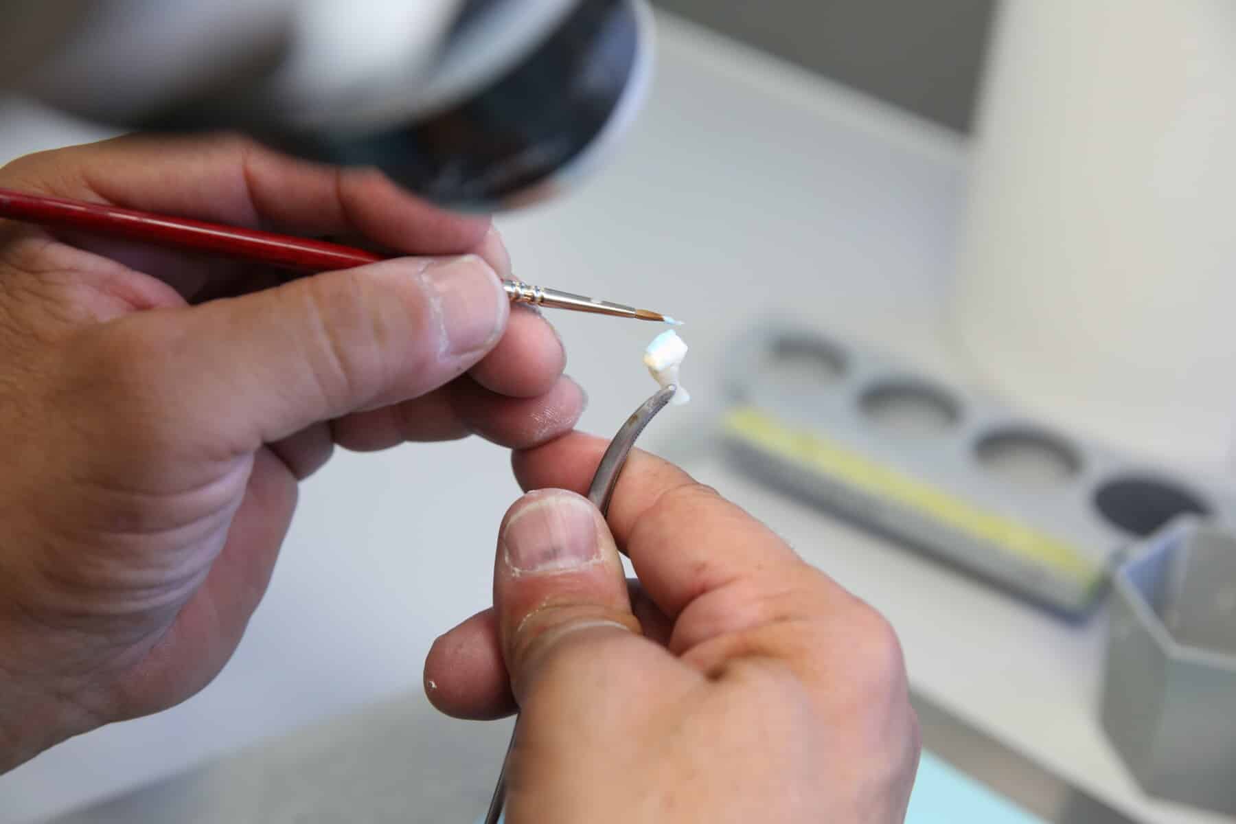 Precision Dental Prosthesis Close-up of John Sanchez, Innova Dental's ceramist, applying delicate porcelain layers to a dental restoration with a fine brush for natural shading.